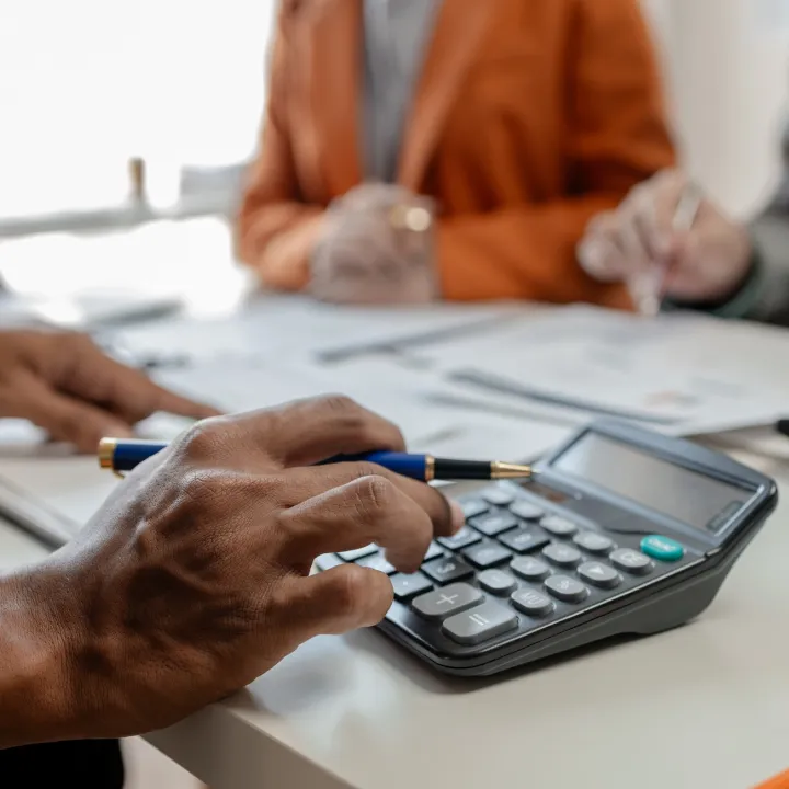 Close up on hands using calculator and writing on a table during a meeting